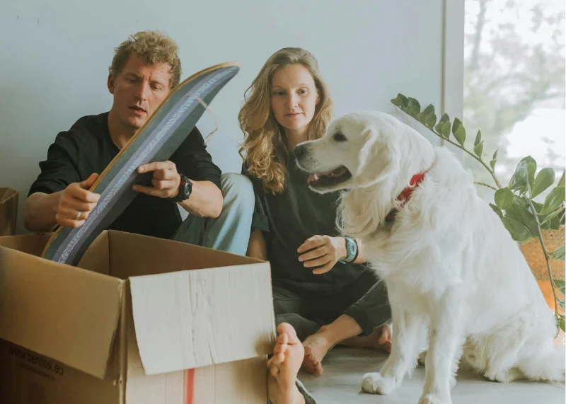 Casal junto a um cão realizando a devolução de um shape de skate.