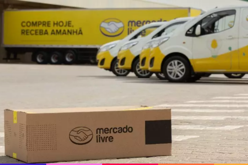 Caixa de encomenda com logo do Mercado Livre e, de fundo, caminhões e carros do serviço logístico do marketplace