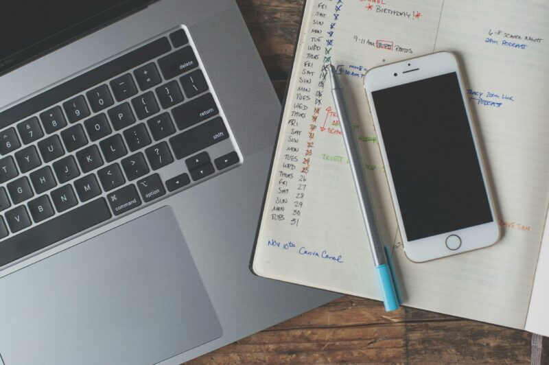 Imagem de um notebook, um celular e um calendário anotado em um caderno simbolizando a organização.