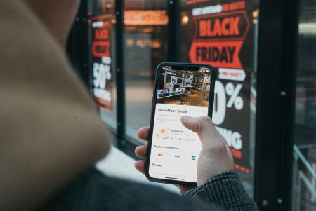 Consumidor consultando informações no smartphone em frente a uma vitrine com anúncio promocional de Black Friday.